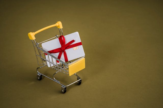 A tiny shopping cart with a white card inside, wrapped in a red ribbon. 